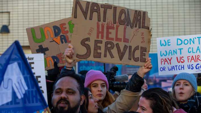 Eine Demonstrantin hält ein Plakat mit der Aufschrift "National Hell Service" hoch.
