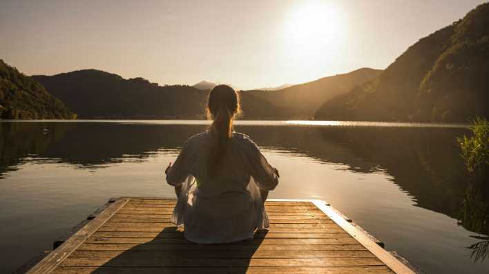 Frau meditiert auf einem Steg am See