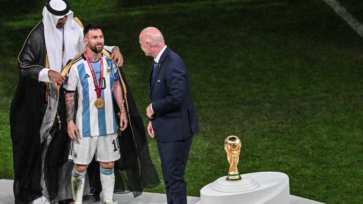 Der Emir von Katar, Scheich Tamim bin Hamad Al Thani, legt Argentiniens Lionel Messi vor Übergabe des Fußball-WM-Pokals vor Fifa-Präsident Gianni Infantino ein Bischt, ein traditionelles arabische Kleidungsstück an.