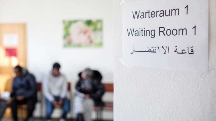 Ein Zettel mit der Aufschrift "Warteraum 1" in mehreren Sprachen hängt an einer Tür.