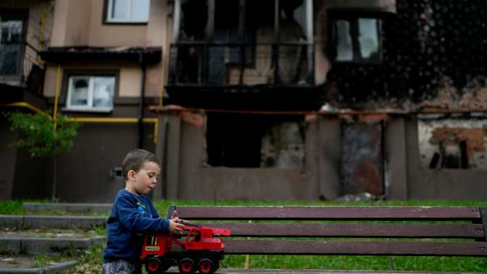 Ein Kind spielt vor einem zerstörten Gebäude.