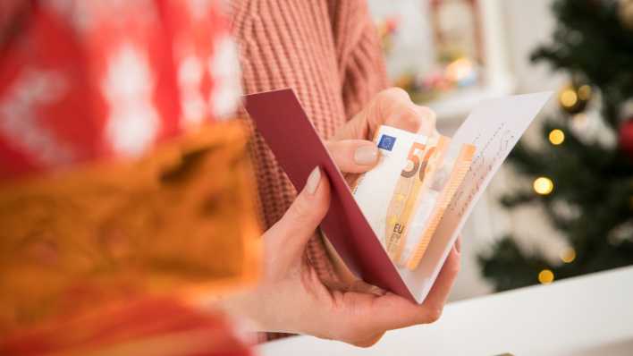 Symbolbild: Eine Frau packt eine Weihnachtskarte mit Geldschein