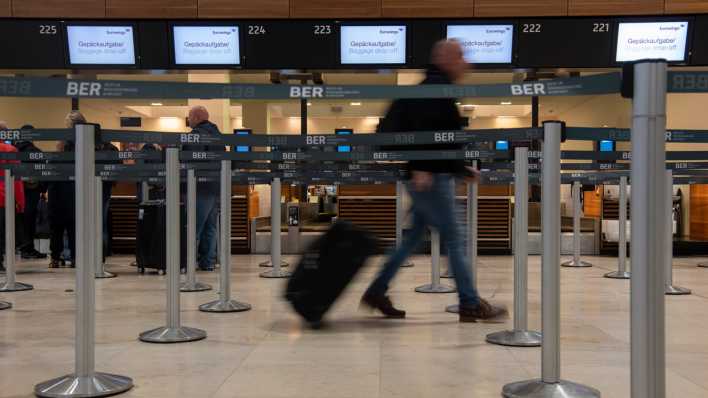 Ein Reisender geht mit einem Koffer zu einem Check-in-Schalter am BER.