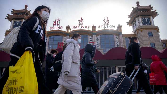 Peking: Reisende mit Mund-Nasen-Schutz gehen mit Koffern an dem Zentralbahnhof vorbei