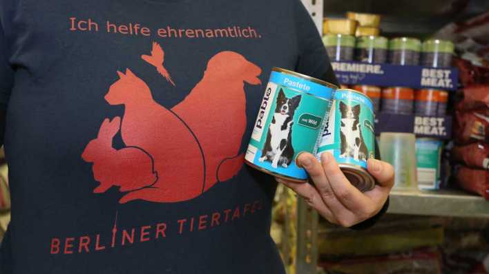 ARCHIV: "Ich helfe ehrenamtlich. Berliner Tiertafel" steht auf dem T-Shirt einer Mitarbeiterin, die in Berlin in einem Raum der Berliner Tiertafel zwei Dosen Hundefutter hält (Bild: picture alliance / dpa)