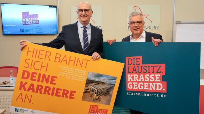 Dietmar Woidke und Klaus Freytag halten Plakate mit der Aufschrift "Hier bahnt sich Deine Karriere an", und "Die Lausitz. Krasse Gegend".