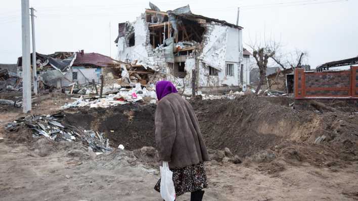 Eine Frau geht an einem zerstörten Haus vorbei.