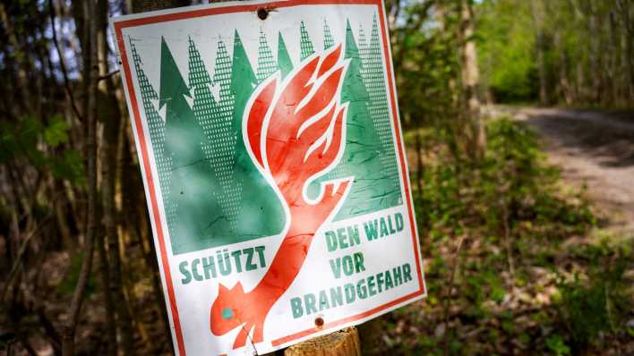 Ein Schild mit der Aufschrift "Schütz den Wald vor Brandgefahr" hängt in einem Wald an einem Waldweg. (Bild: picture alliance/ dpa)