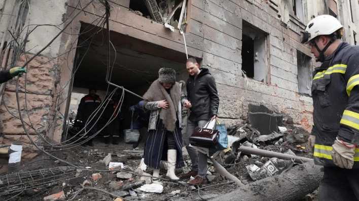 Ein Mann hilft einer Frau beim Verlassen eines Wohnhauses, das von einer russischen Rakete getroffen wurde.