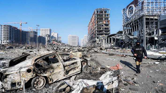 Ein Polizeibeamter steht neben der Ruine eines Einkaufszentrums, dass durch einen russischen Raketenangriff zerstört wurde.