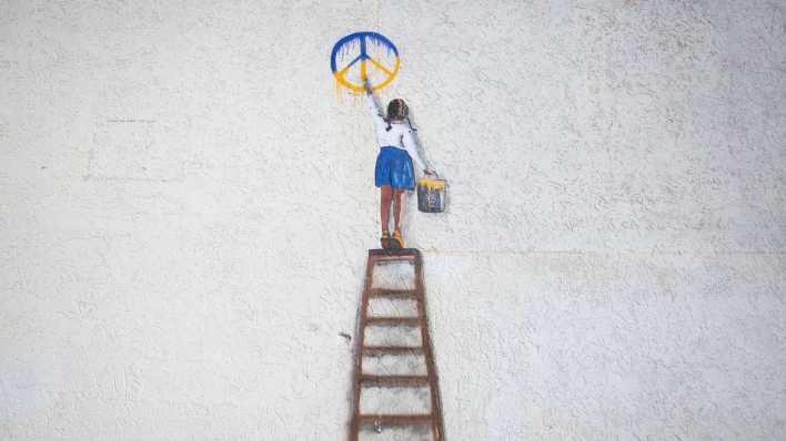 Ein Graffiti des italienischen Künstlers Tvboy in Bucha zeigt ein Mädchen, das ein Friedenszeichen an eine Wand malt.