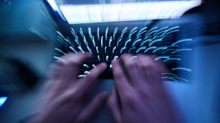 Ein Mensch sitzt wie ein Hacker in einem dunklen Zimmer vor einem Computer. (Quelle: Picture Alliance)