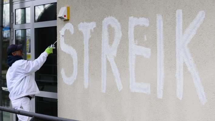 Maler überdecken einen schwarzen Schriftzug "Streik" mit weißer Farbe.