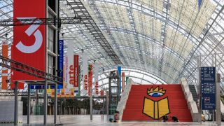 Eine Werbetechnikerin und ein Werbetechniker kleben das Logo der Leipziger Buchmesse auf eine Treppe in der Glashalle der Leipziger Messe.