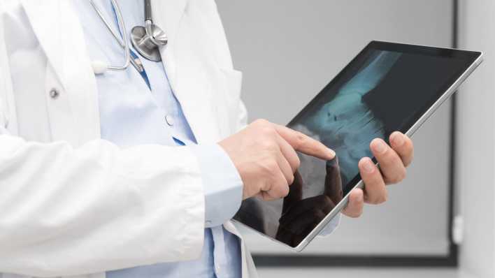 Ein Arzt hält ein Tablet in der Hand. Darauf ist ein Röntgenbild zu sehen (Bild: picture alliance / Zoonar )