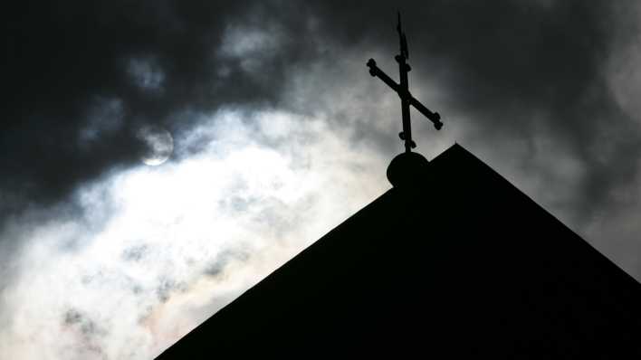 Symbolbild Missbrauch in der Kirche - Im Gegenlicht und vor wolkenverhangenem Himmel ist die Kirchturmspitze des Doms mit Kreuz zu sehen (Bild: picture alliance / dpa)