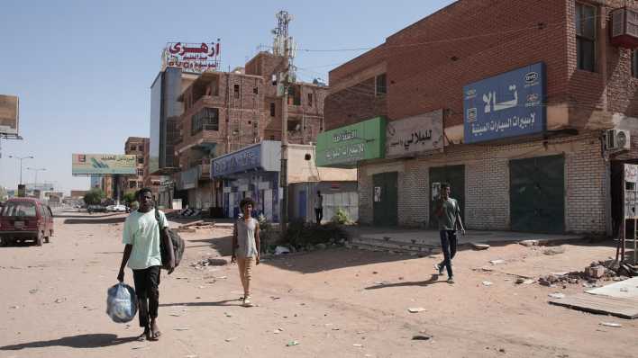 Menschen in der sudanesischen Hauptstadt Khartum gehen an verschlossenen Geschäften vorbei. (Bild: picture alliance/dpa/AP)
