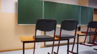 Kreidetafel einer Schule. Im Vordergrund sind Tische und Stühle zu sehen. (Bild: IMAGO / Fotostand)
