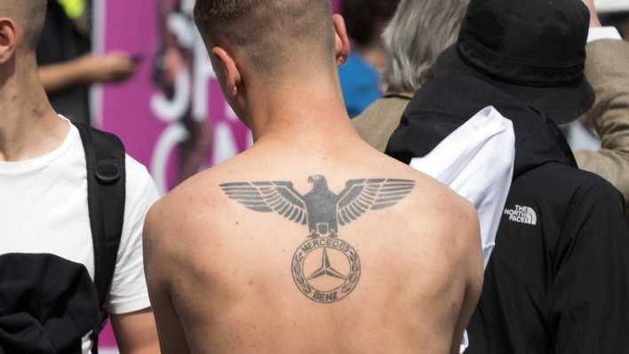 Teilnehmer an einer Neonazi-Demo entblößt seinen Rücken mit Tattoo