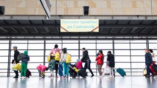 Geflüchtete aus der Ukraine laufen nach ihrer Ankunft durch die Eingangshalle vom Messebahnhof Laatzen. Auf einem Banner im Hintergrund steht "Willkommen in Hannover" auf Ukrainisch.