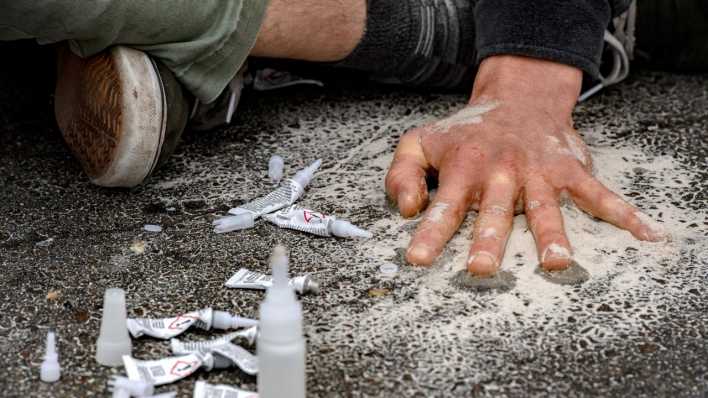 Ein Demonstrant klebt sich bei einer Straßenblockade der Letzten Generation mit einer Hand auf die Straße