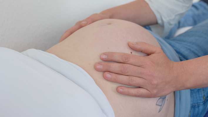 Eine Hebamme untersucht in einem Geburtshaus den Bauch einer werdenden Mutter.
