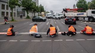 Bei einer Straßenblockade der Letzten Generation sitzen Aktivisten auf dem Mühlendamm auf der Straße