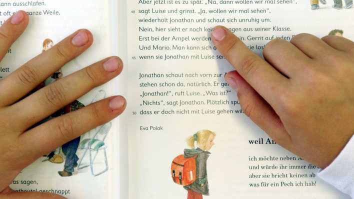 Buchstabe für Buchstabe gleiten die Finger eines Schülers über die Buchseite beim Deutschunterricht der dritten Klasse