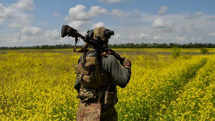 Ein ukrainischer Soldat läuft mit seinem Gewehr auf der Schulter durch ein Rapsfeld.