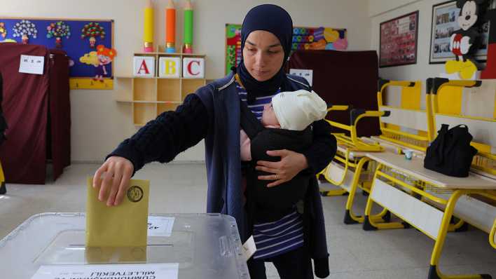 Eine Frau mit einem Baby auf dem Arm wirft ihren Stimmzettel in einem Wahllokal in Ankara in eine Wahlurne.