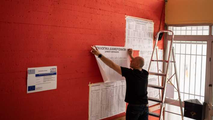 Ein Mitarbeiter hängt Kandidaten- und Parteilisten an die Wand eines Wahllokals in Griechenland.