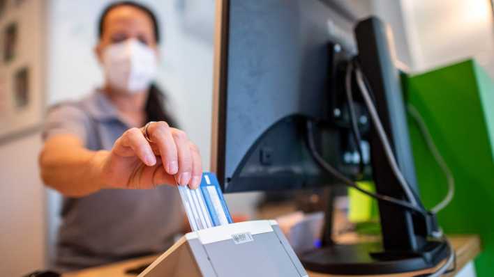 Eine Medizinische Fachangestellte schiebt die Versichertenkarte eines Patienten in das Lesegerät.