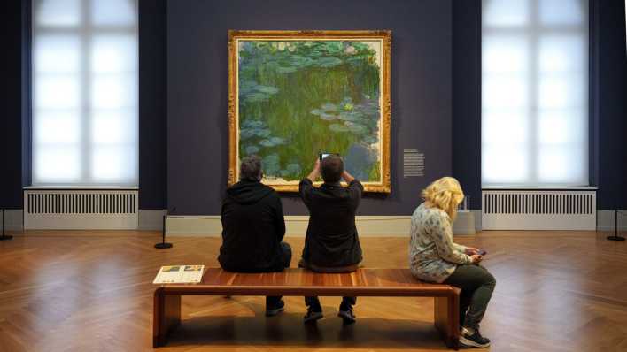 Besucher sitzen im Museum Barberini vor dem Bild "Seerosen" (1914 bis 1917) von Claude Monet auf einer Bank.