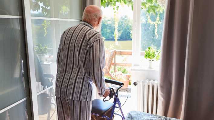 Senior als Patient im Schlafanzug mit Gehhilfe blickt aus dem Fenster in der Reha Klinik