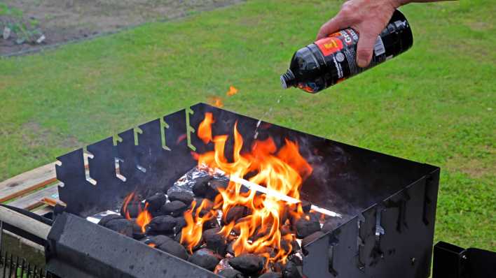 Ein Mann riskiert schwerste Brandverletzungen in dem er Brandbeschleuniger aus einer Flasche auf glühende Holzkohle schüttet.