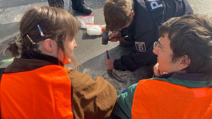 Polizist versucht, Demonstranten Hannah und Markus der "Letzten Generation" von der Straße abzulösen