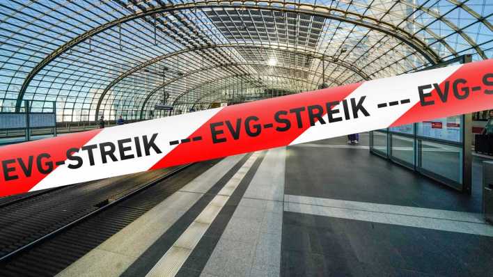 Ein symbolisches, stilisiertes Flatterband in Rot-Weiß mit der Aufschrift "EVG-STREIK" vor einer Szene im relativ leeren Berliner Hauptbahnhof (Bild: picture alliance / SULUPRESS.DE)