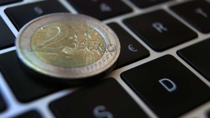 Symbolbild: Eine Zwei -Euro-Münze liegt auf der Tastatur eines Laptops neben einem Eurozeichen