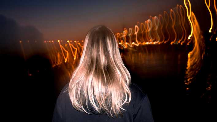 Symbolbild: Blonde Frau von hinten bei Nacht mit Licht