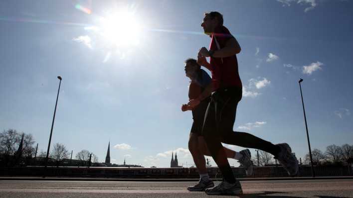 Jogger laufen bei direkter Sonneneinstrahlung auf einem Weg.