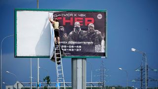 Ein Mann nimmt an einer Autobahn am Stadtrand von St. Petersburg das Plakat mit der Aufschrift "Schließt euch uns bei Wagner an" ab