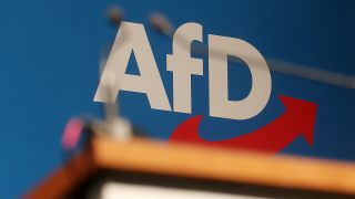 Ein Schild mit den Buchstaben AfD steht hinter einem Rednerpult (Bild: dpa / David Young)