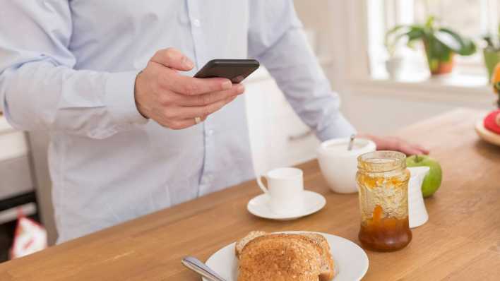 Mann mit Handy am Frühstückstisch