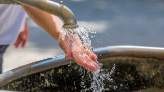 Eine Frau kühlt ihre Hand n einem Wasserspielplatz.