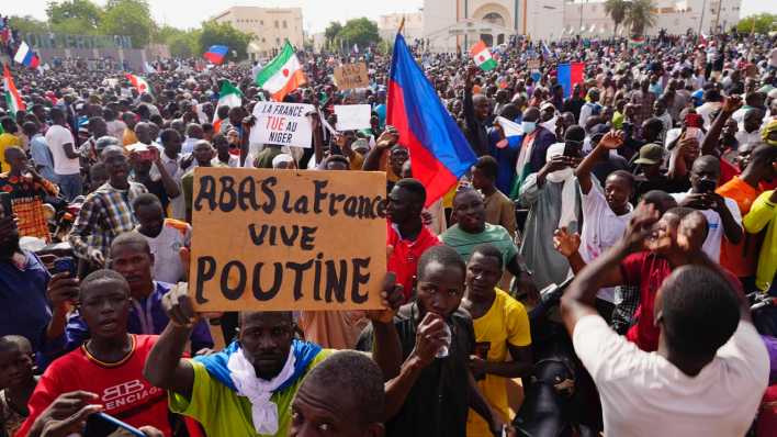 Menschen halten Plakate und Fahnen während sie an einem Marsch teilnehmen, zu dem Anhänger des Putschisten General Omar Tchiani im Niger aufgerufen haben.