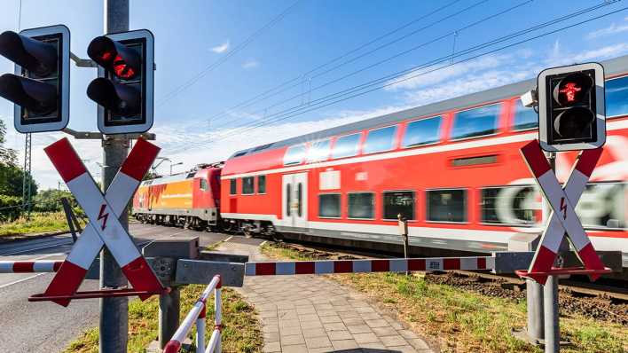 Eine Schranke ist an einem Bahnübergang in Lübbenau geschlossen, wärend ein Regionalzug vorbeifährt.