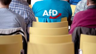 Ein Mann mit einem T-Shirt mit AfD-Logo sitzt während des Landesparteitags der Alternative für Deutschland Hessen im Haus der Begegnung im Publikum.