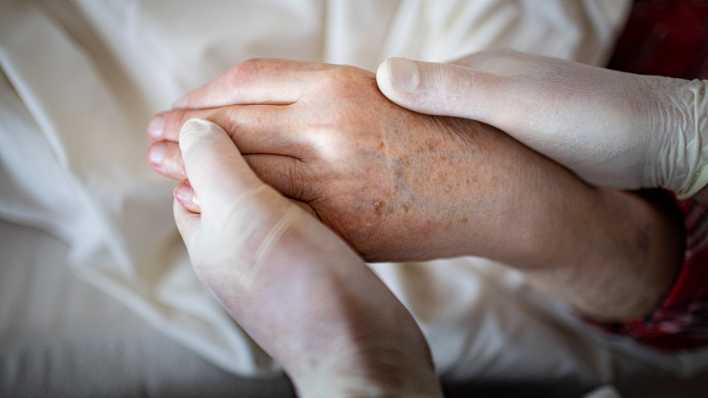 Die Hand eines älteren Menschen wird von zwei Händen in medizinischen Handschuhen gehalten (Bild: picture alliance / Ute Grabowsky)