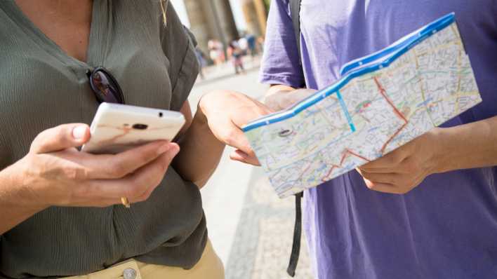 Eine Frau und ein Mann stehen in Berlin vor dem Brandenburger Tor und schauen auf ein Handy
