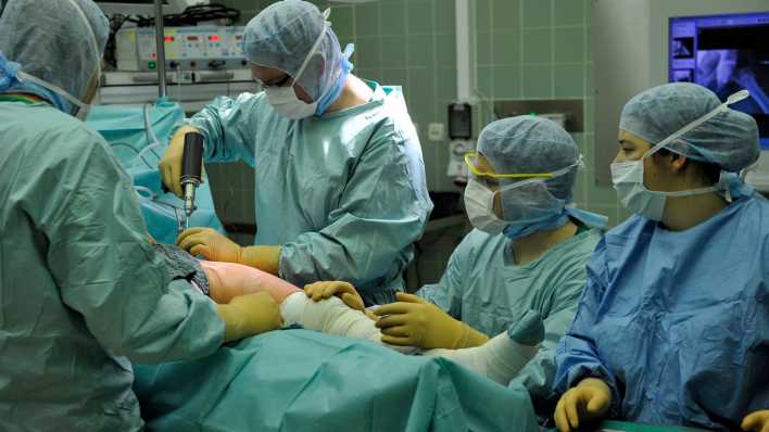 Ein Operationsteam arbeitet bei einer Hüftoperation am Operationstisch.